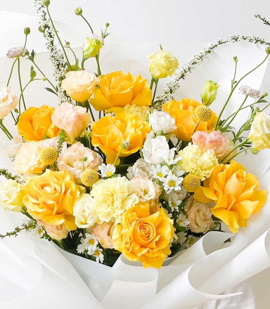 Bright yellow roses and ranunculus graduation bouquet with white paper wrap