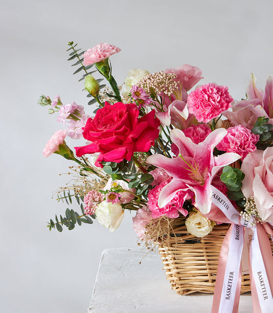 Vibrant pink and red roses with fuchsia lilies in woven basket, birthday flower gift with satin ribbons