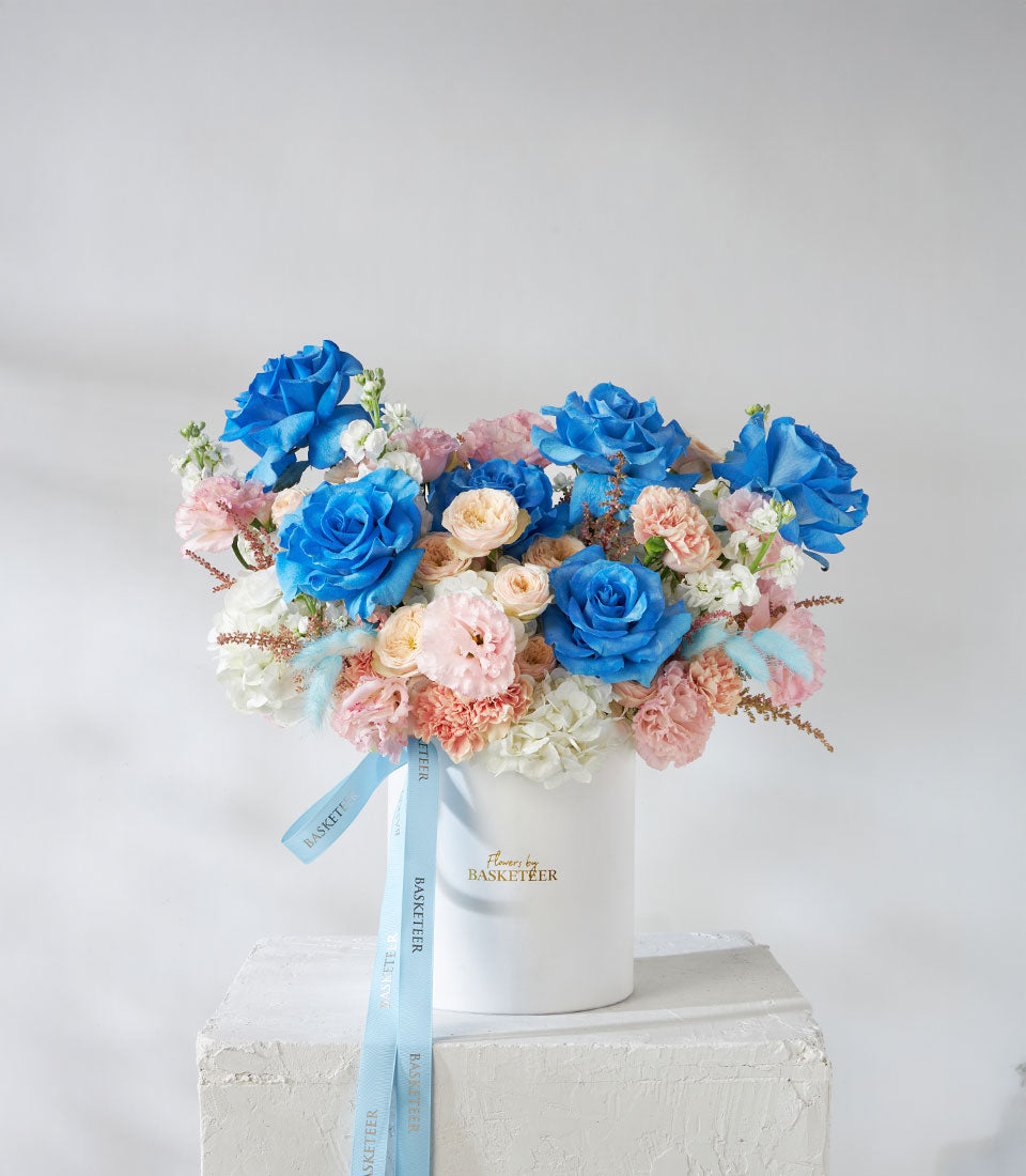 Tinted blue and pastel roses with carnations in white cylindrical gift box