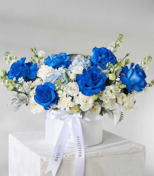 Tinted blue roses and white carnations in elegant white hatbox with satin ribbon