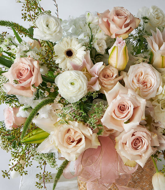 Quicksand roses and white lilies in woven luxury gift basket with fresh greenery