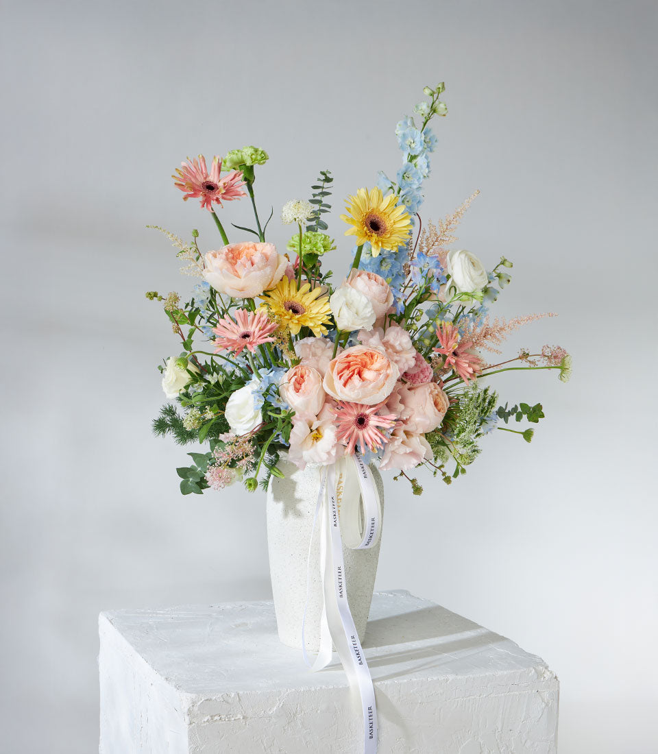 Pastel garden roses and gerbera daisies in white ceramic vase with fresh greenery
