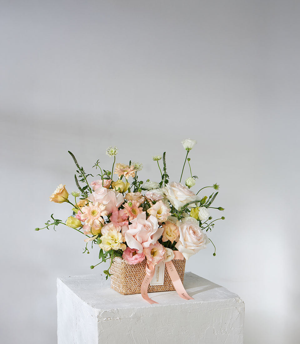 White O'Hara and pink Mondial roses with lisianthus in a woven pastel flower basket with ribbon bow