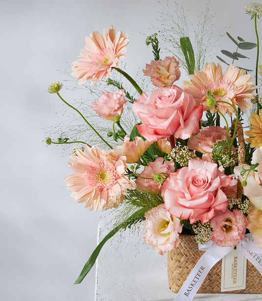 Pastel pink and peach roses with gerbera daisies in woven basket, fresh flower gift for birthday