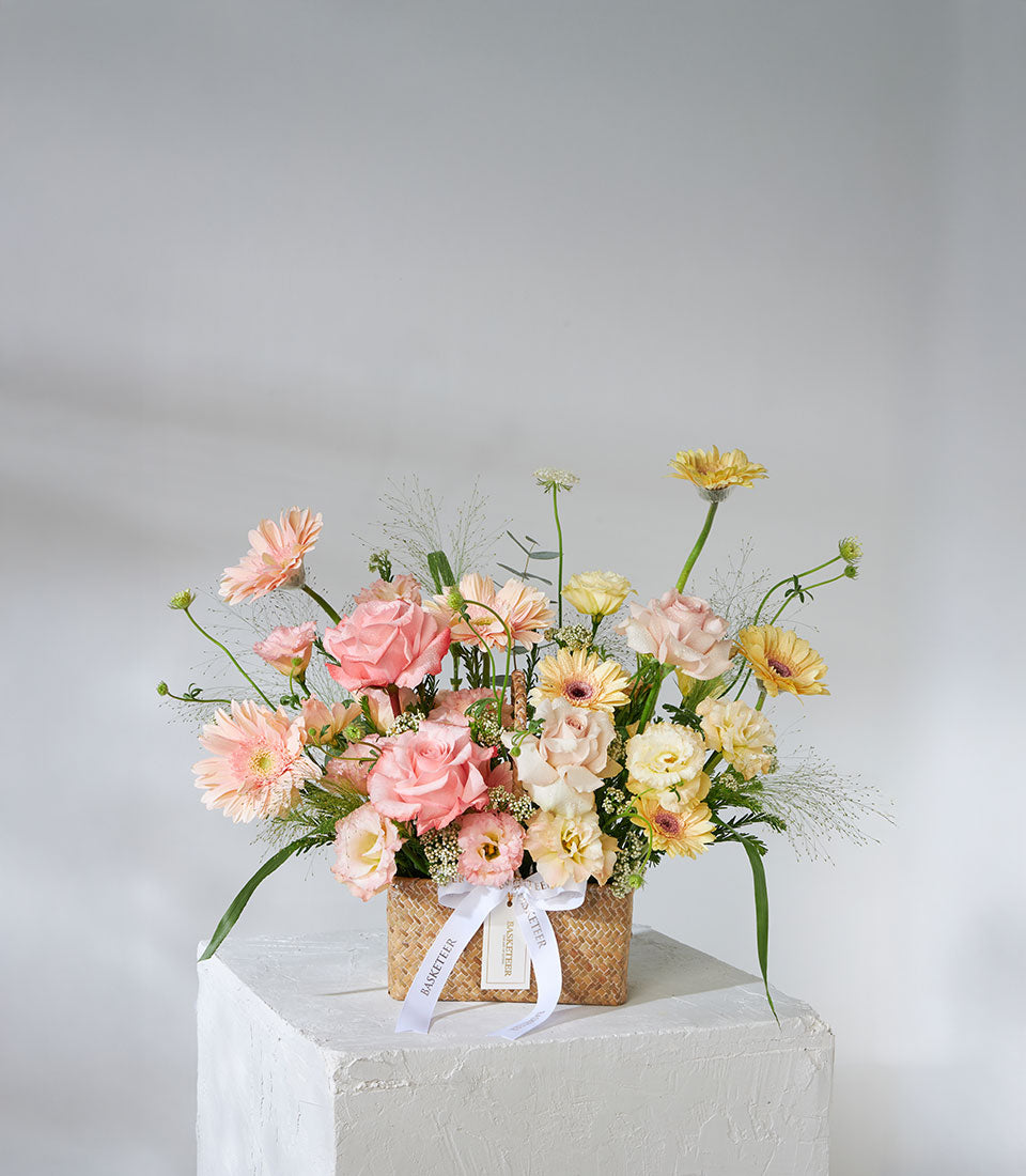 Pastel pink, peach, and yellow rose bouquet with gerberas in woven basket, perfect for birthday gifts