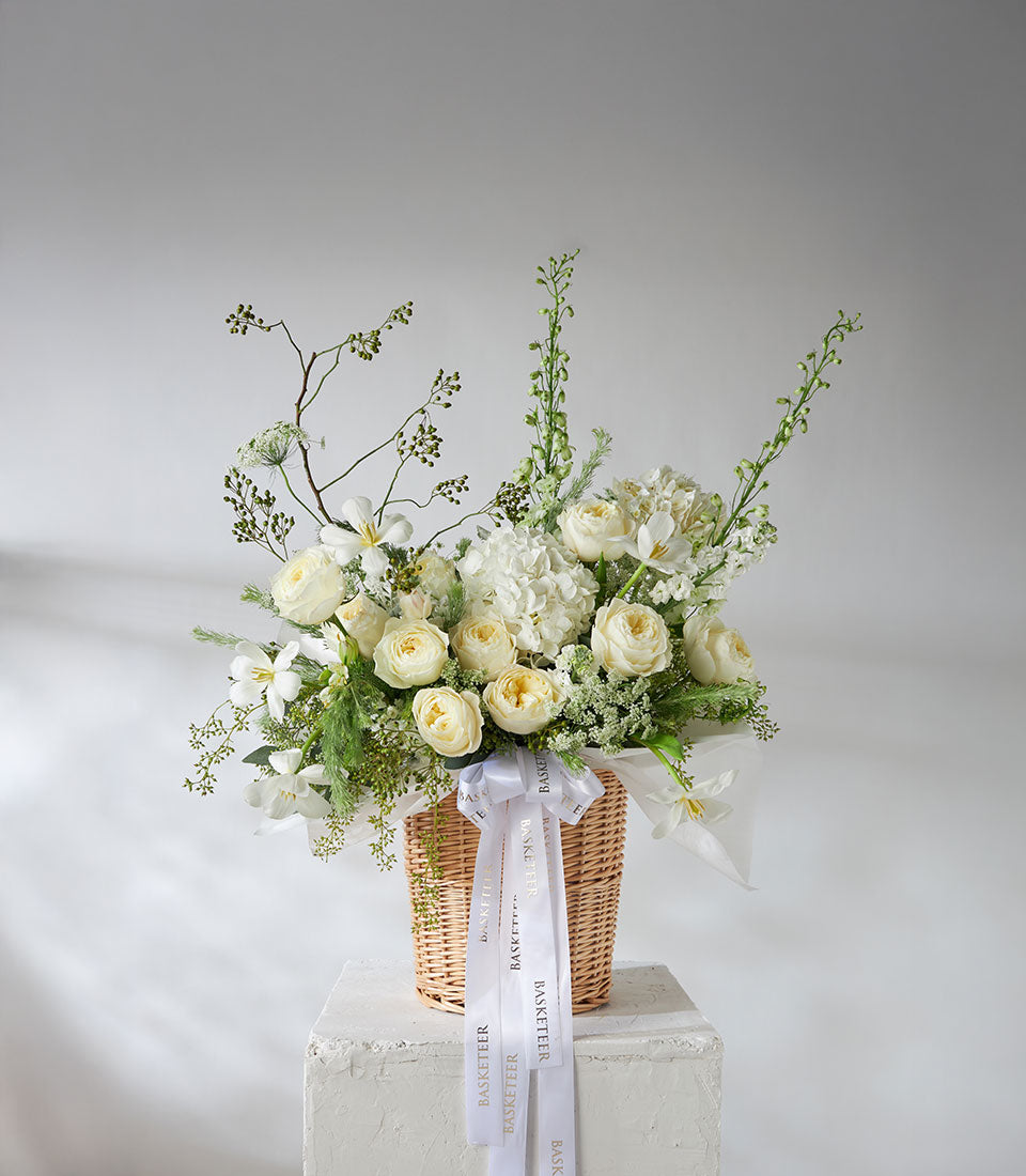 Elegant white roses and hydrangea arrangement in woven basket with satin ribbon