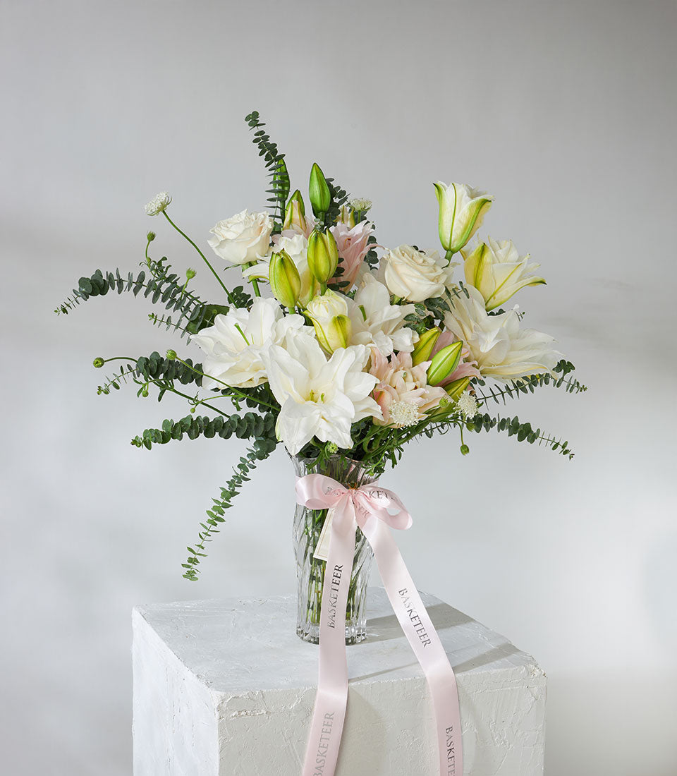 White and pink roses with lilies in crystal vase, tied with pink ribbon
