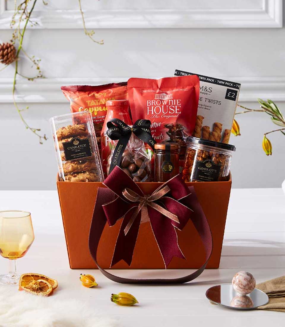 Premium gourmet hamper with imported chocolates, brownies, and artisan treats in maroon-ribboned orange box, New Year gift