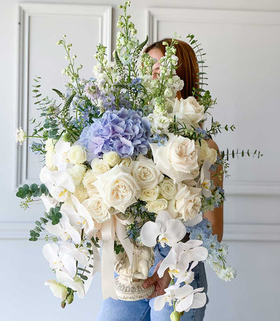 White ceramic vase ensemble with white roses, blue hydrangeas, and orchids in luxury gift arrangement