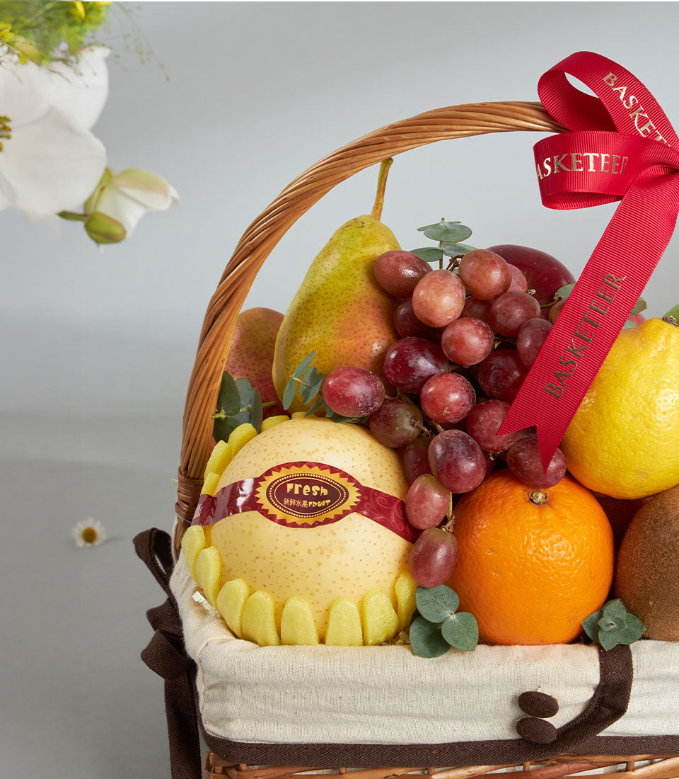 Woven fruit basket with fresh red apples, pears, grapes, oranges and kiwi, cream linen lining, brown trim