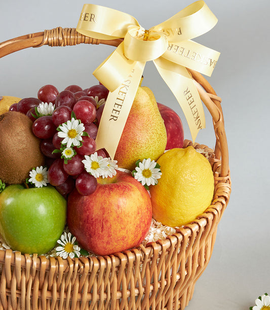 Wicker fruit basket with mixed fresh fruits, white daisies, and gold-stamped yellow satin ribbon