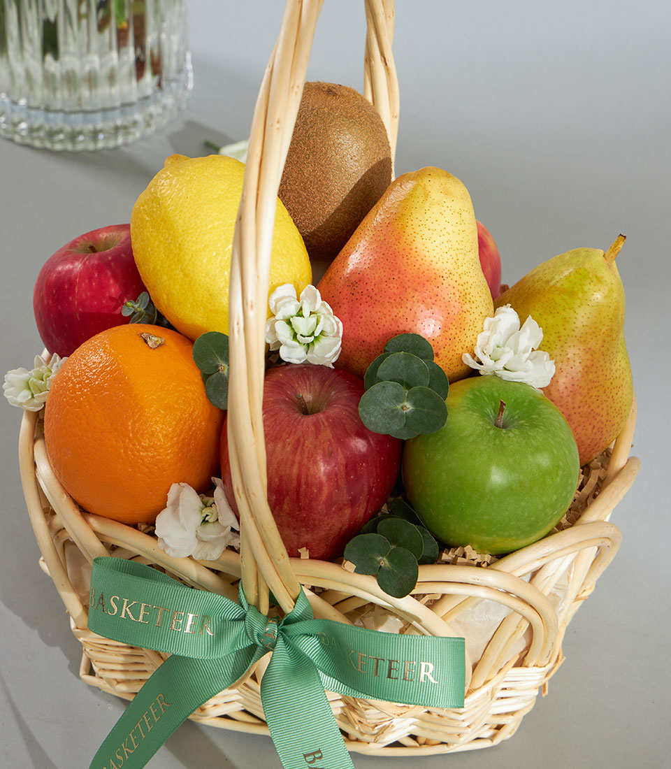 Light wicker basket overflowing with fresh imported fruits, white flowers and eucalyptus, tied with green ribbon