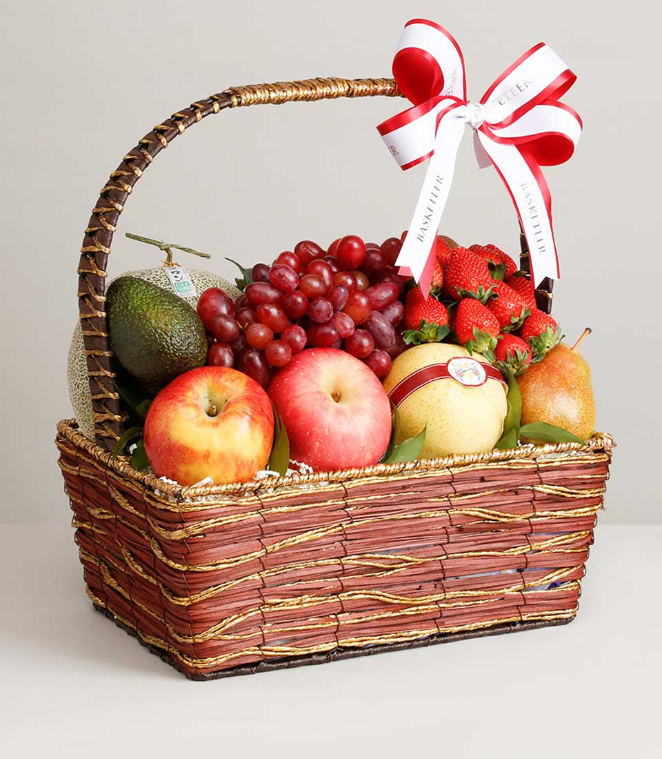Woven fruit basket with grapes, strawberries, apples, avocado, melon and pears on white filler
