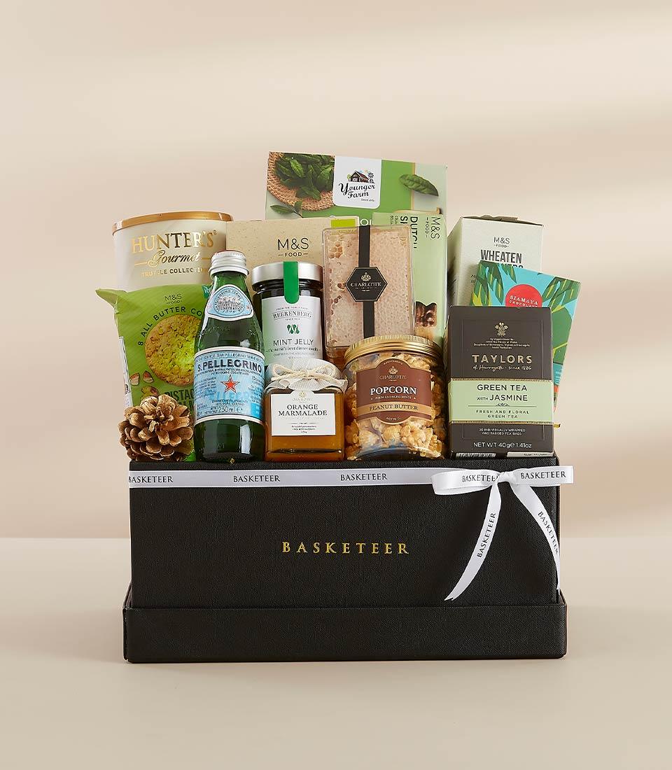Premium gourmet gift hamper with sparkling water, preserves, tea, and crackers in black box with white ribbon