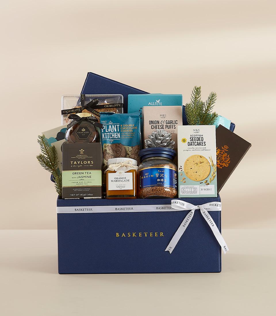 Navy blue gourmet hamper with green tea, marmalade, coffee, chocolate cookies, and Scottish oatcakes, tied with white ribbon