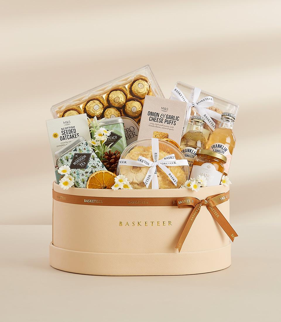 Round beige luxury gift hamper with Scottish oatcakes, gourmet chocolates, tea, and tropical treats for New Year gifting