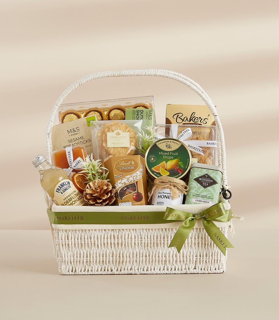 White wicker gourmet gift basket with artisan treats, chocolates, and premium beverages tied with dark green ribbon for New