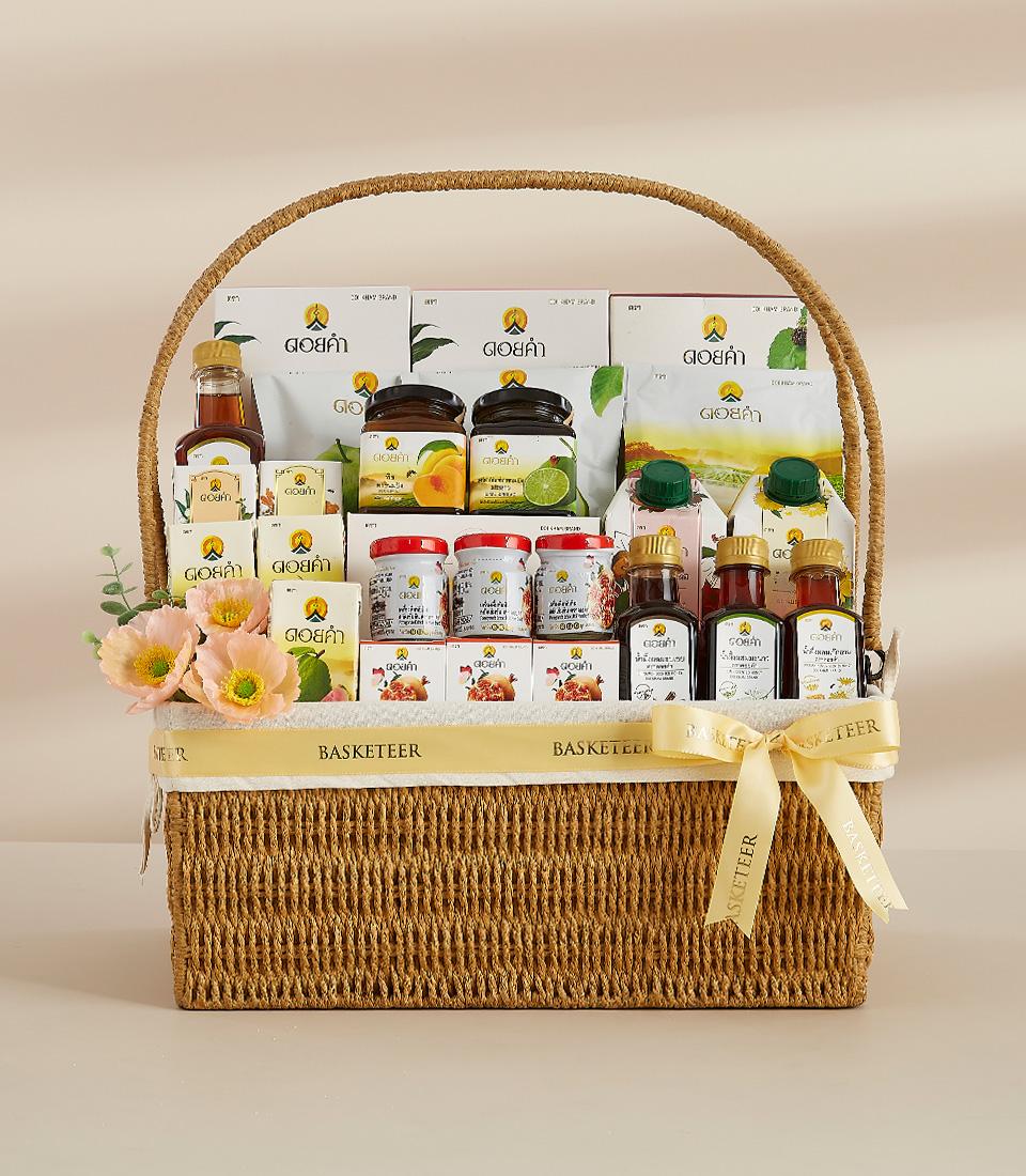 Woven gift basket filled with Thai herbal products, golden-capped bottles, and fruit preserves with cream Basketeer ribbon