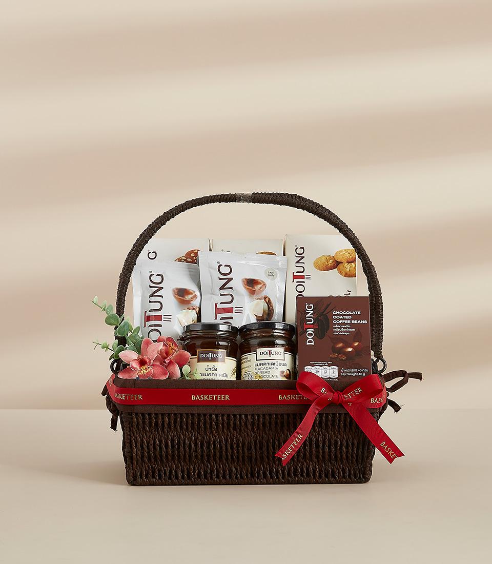 Dark woven gift basket with Thai gourmet treats, honey jar, macadamia spread, and fresh flowers with red ribbon bow