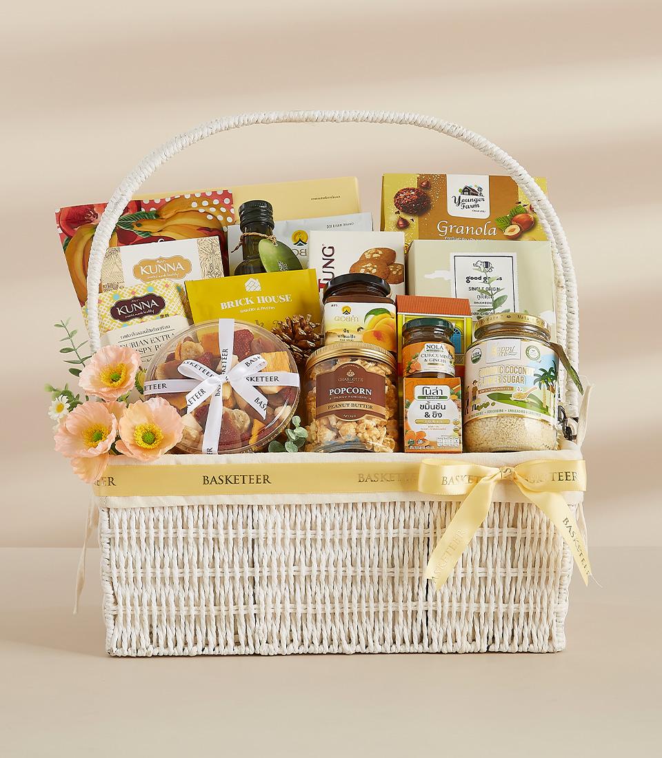 Taste of Thailand white wicker gift basket with gourmet snacks, granola, and peach flowers for New Year gifting