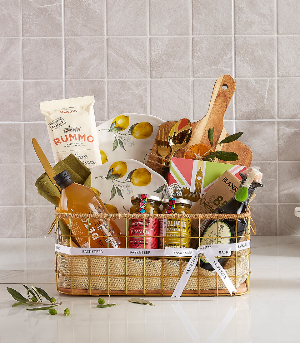 Elegant Mediterranean gourmet gift basket with ceramic plates, pasta, olives, olive oil, and gold cutlery in gold wire