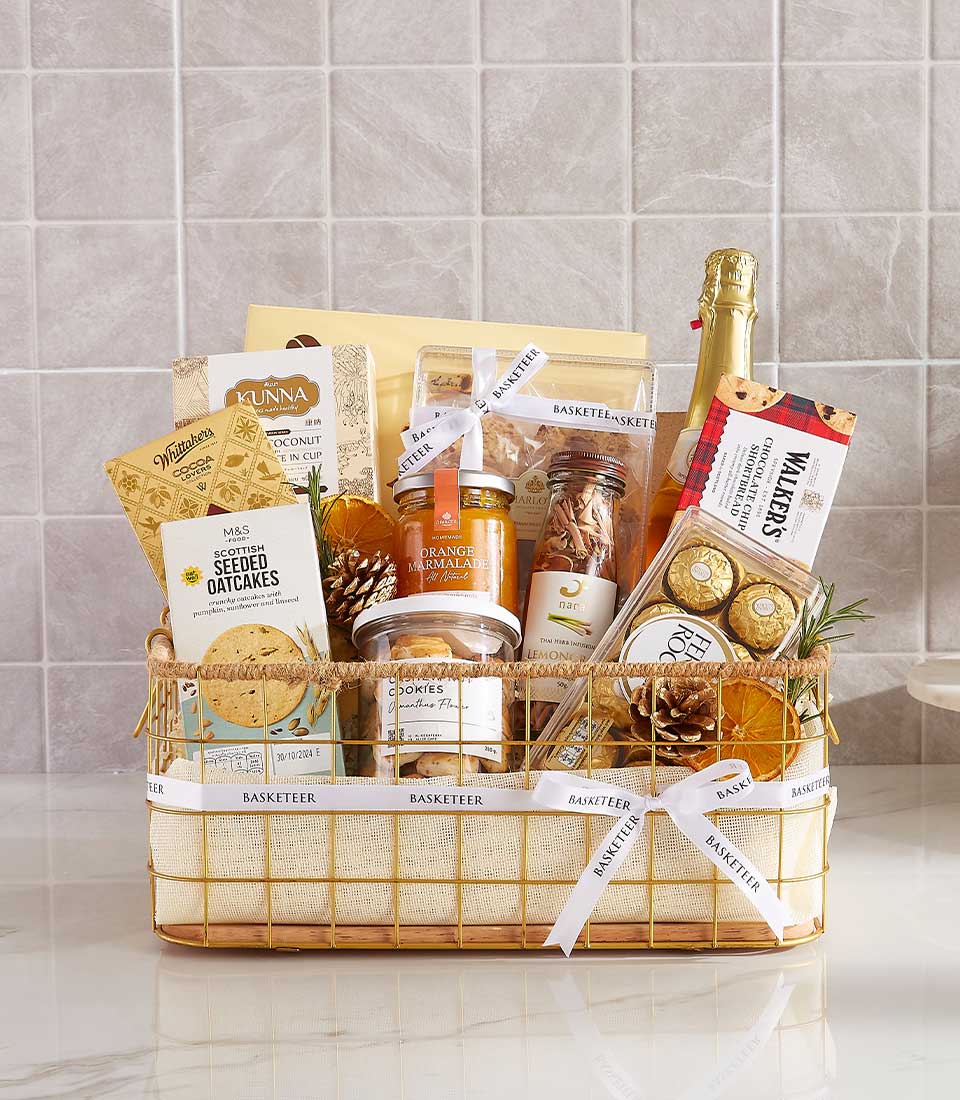 Luxury gourmet gift basket with sparkling wine, chocolates, and artisan treats in gold-toned wire frame, tied with white