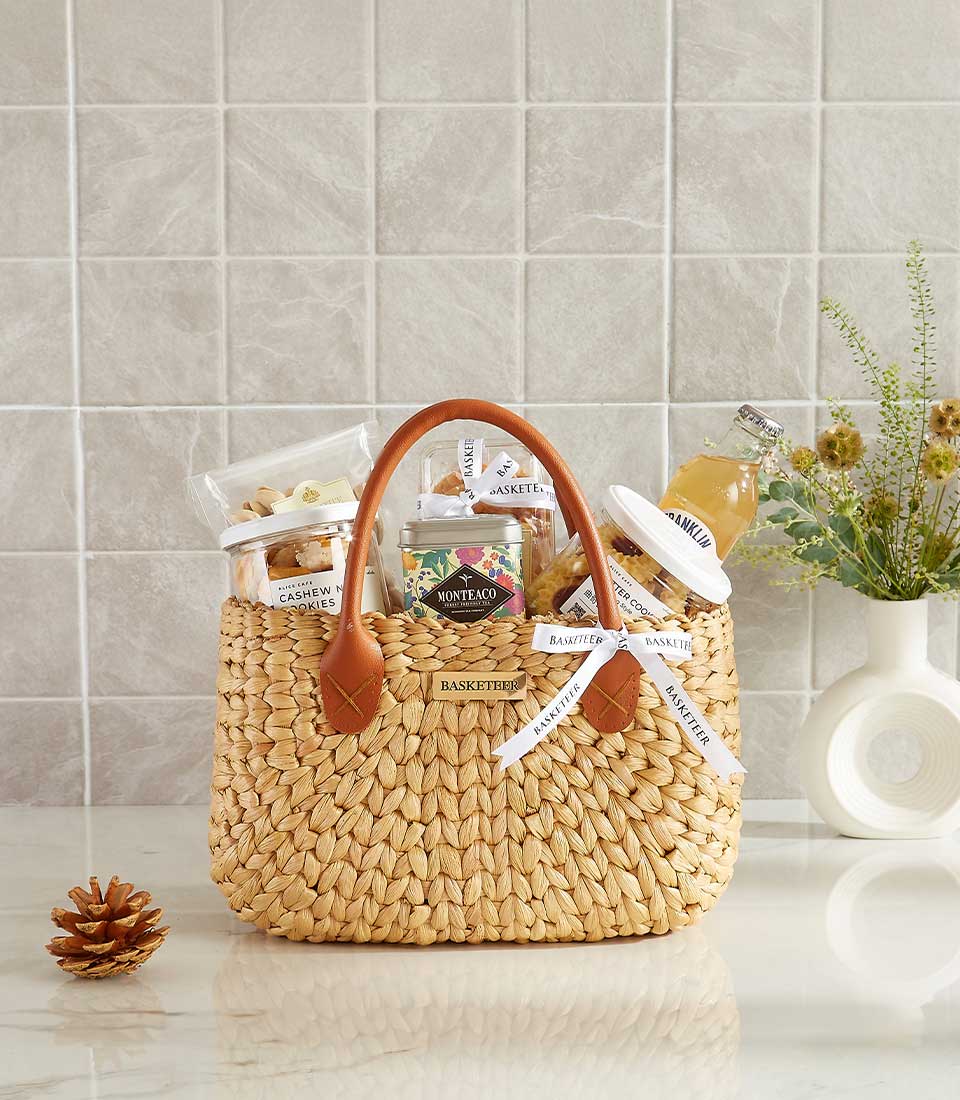 Woven straw gift basket with leather handles filled with gourmet treats, tea, and wellness items for New Year gifting