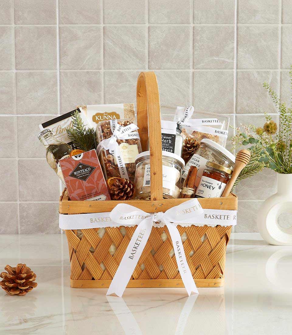 Woven wood gourmet gift basket with olive oil, tea, nuts, honey, and artisan treats tied with white ribbon