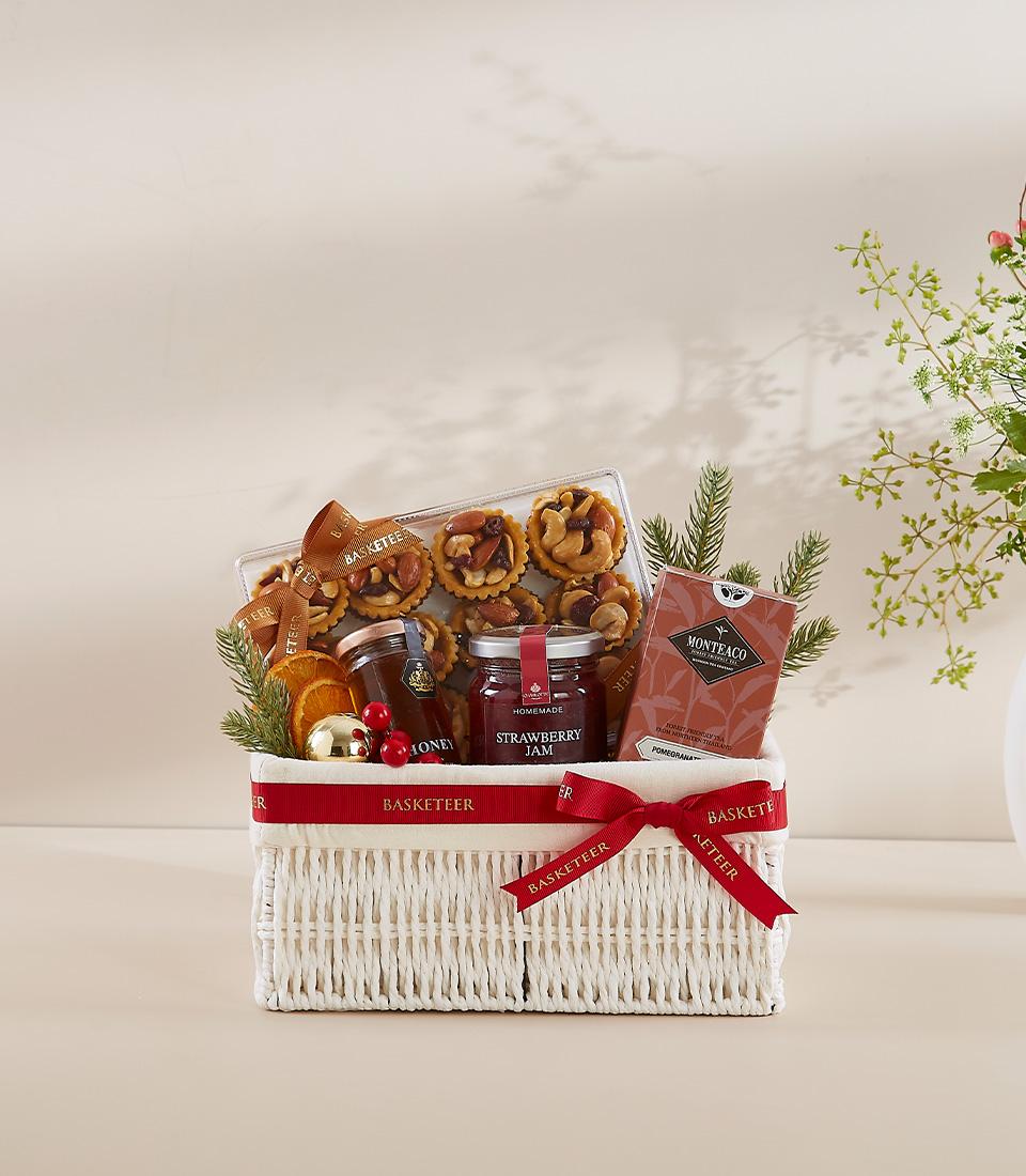 Basketeer premium hamper delivery Thailand: Wicker gift basket with gourmet tarts, honey, strawberry jam, and fragrant tea. Tied with a festive red ribbon.