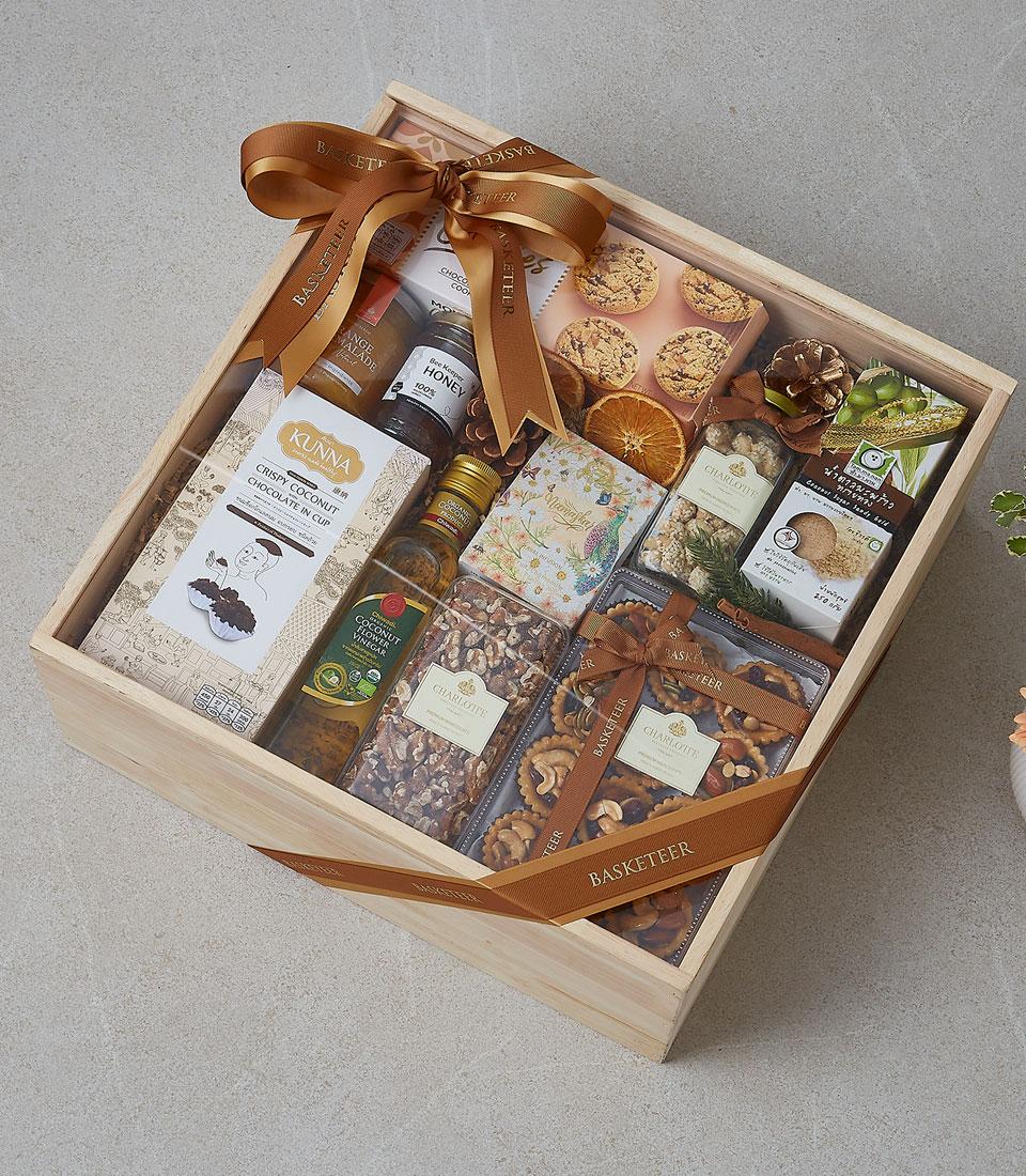 Wooden gift box filled with gourmet treats including honey, coconut vinegar, chocolate, cookies and nuts, tied with