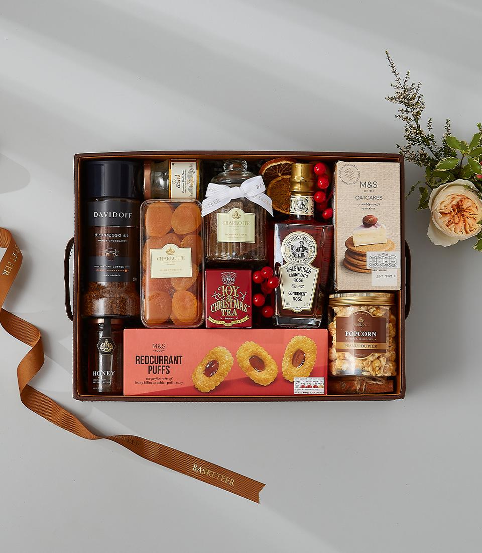 Luxury gourmet gift hamper with coffee, honey, tea, and artisan treats in dark brown leather box with peach rose bouquet