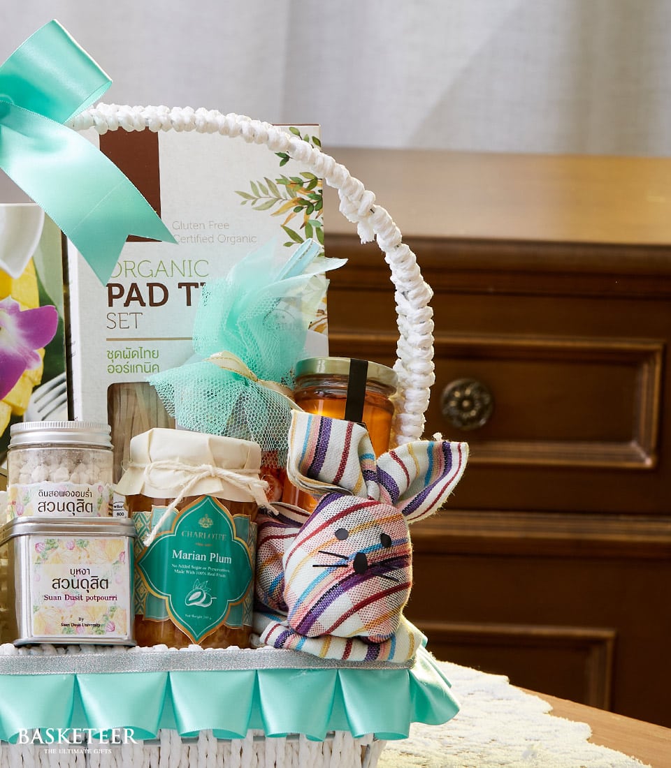 Luxury white gift basket with light blue satin ribbon, organic Thai pad thai set, Marian plum jam, and artisan goods for