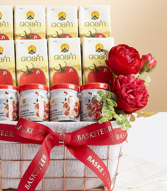 Rose gold wire mesh gift basket with Doi Kham tomato juice cartons, pomegranate jars, and fresh red flowers