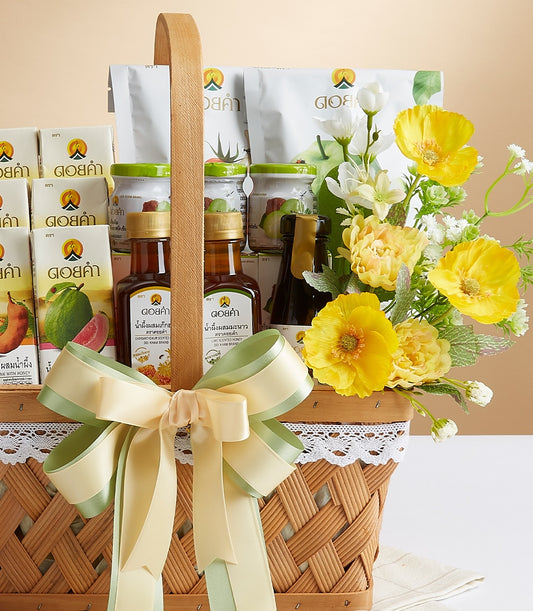 Woven gift basket with Doi Kham juice boxes, bottled wellness drinks, and preserved fruit jars, dressed with pale green