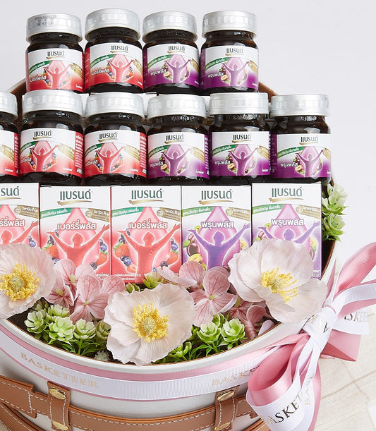 Premium health wellness gift basket with bottled beverages, white ceramic container, leather straps, and fresh pink and
