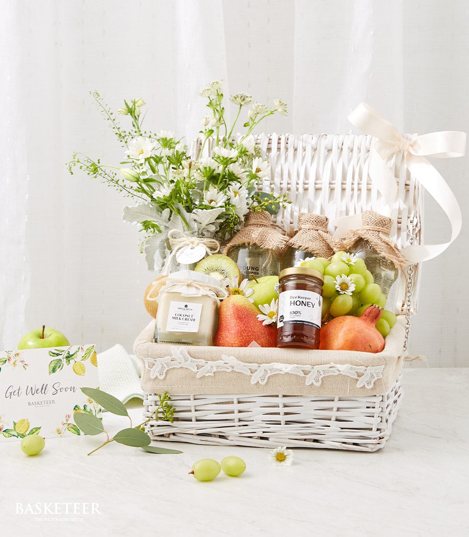 Woven white wicker get well fruit hamper with fresh grapes, kiwi, pears, honey, and white flowers