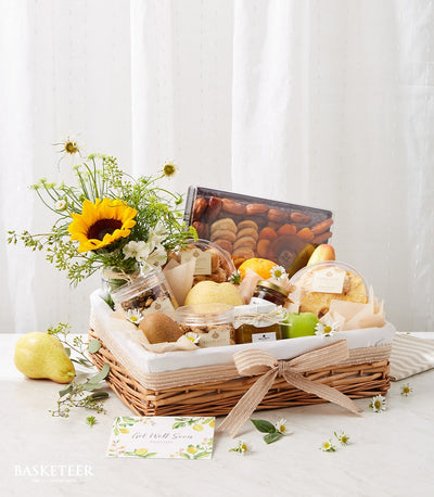 Wicker gift basket with dried fruits, fresh produce, gourmet jars, and yellow sunflower bouquet for get well recovery