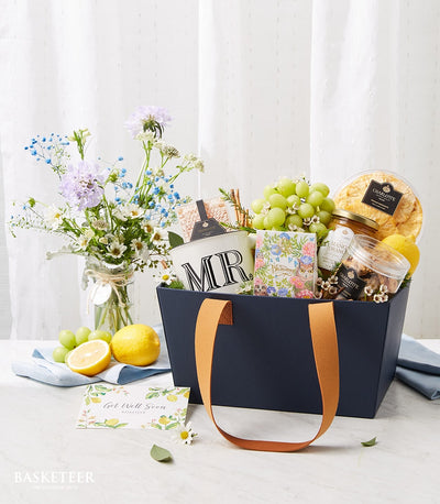 Navy gift basket with fresh fruits, mango preserve, cookies, white mug, and cheerful get well soon card for recovery