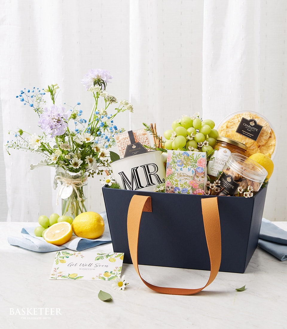 Navy gift basket with fresh fruits, mango preserve, cookies, white mug, and cheerful get well soon card for recovery