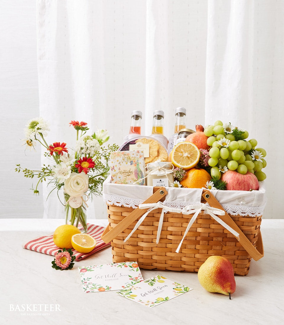 Wicker fruit basket with fresh citrus, grapes, beverages, and white-red flower bouquet for get well recovery gift