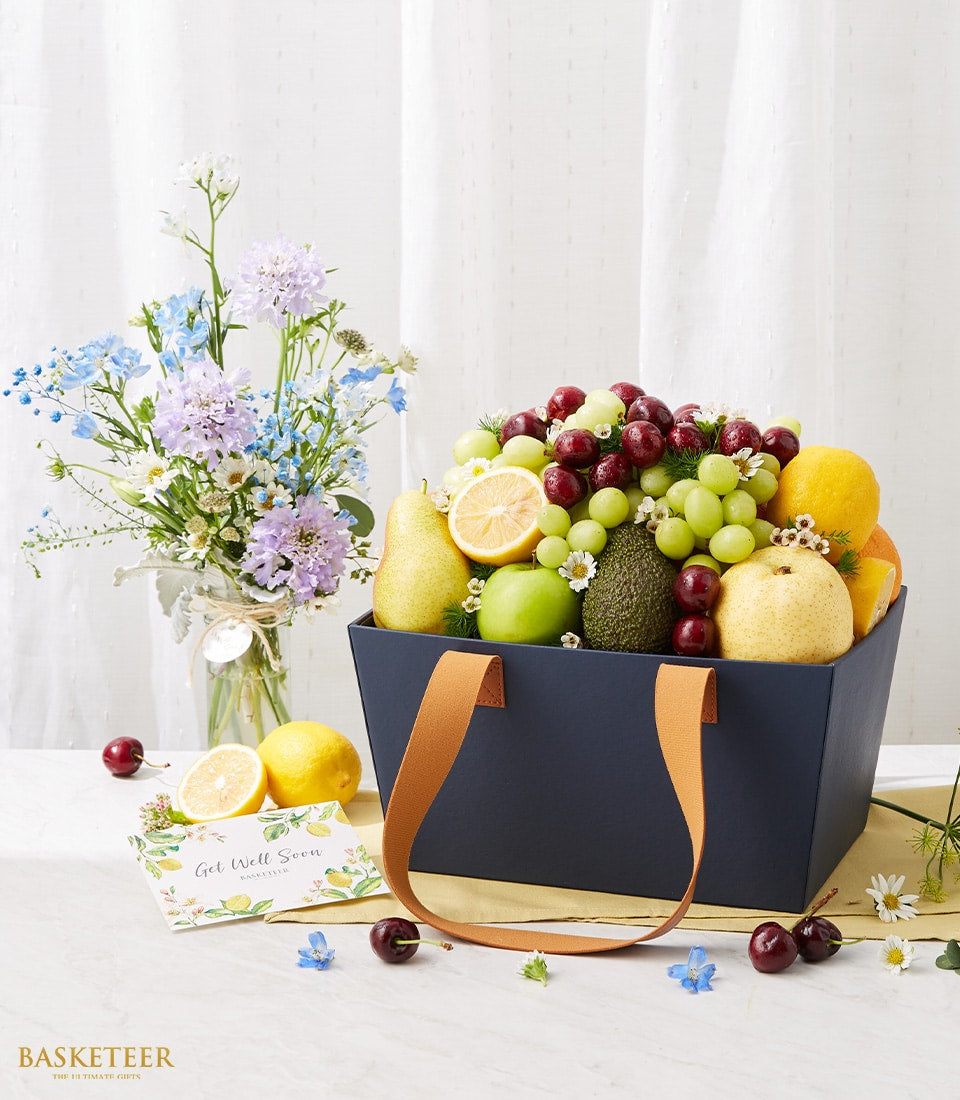 Navy fruit basket with fresh cherries, grapes, pears and mixed blooms, paired with delphinium and scabiosa arrangement for