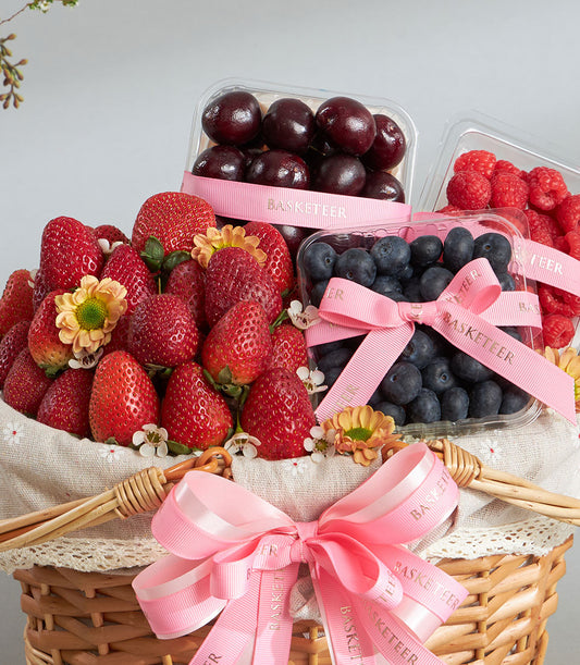 Luxury fresh berry basket with strawberries, cherries, blueberries, raspberries in woven wicker with pink ribbon