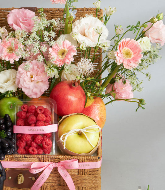 Woven wicker basket with pink pastel flowers, fresh fruit, and ribbon bow for gifting