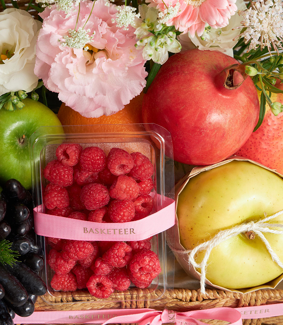 Premium fruit and pink floral gift basket with fresh raspberries, citrus, pomegranate, and carnations in wicker