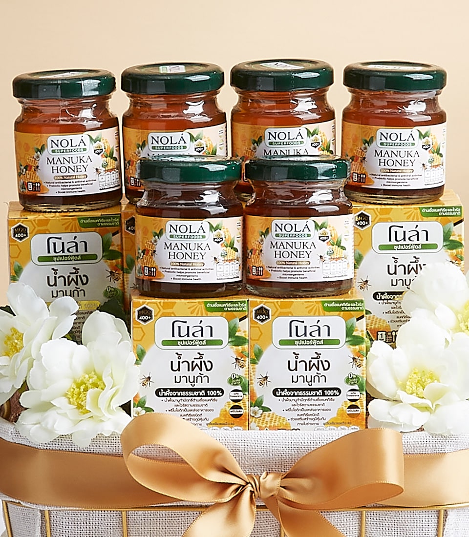 Nola Superfood Manuka honey gift basket with golden amber jars, green lids, and golden satin ribbon bow