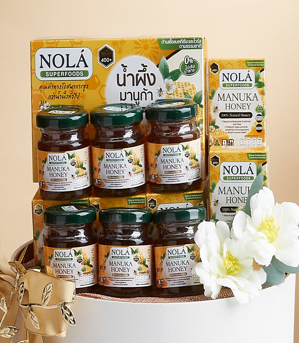 Nola Manuka Honey gift set with nine glass jars, gold ribbon, and white flowers in premium basket