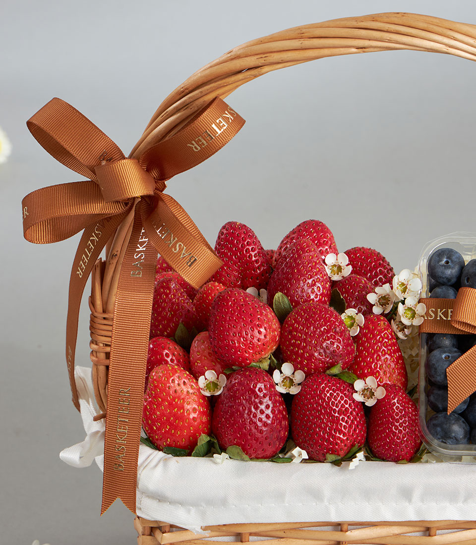 Premium strawberry and blueberry wicker gift basket with fresh berries, white flowers, and brown ribbon bow