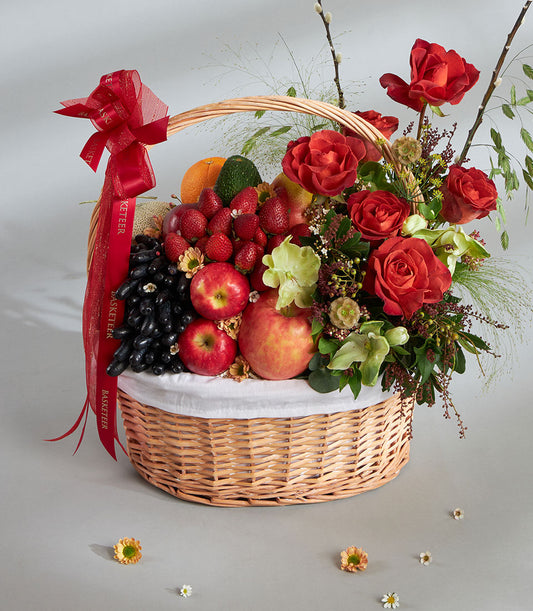 Basketeer premium hamper delivery Thailand: Wicker basket overflowing with grapes, strawberries, apples, and red roses. Tied with a luxurious red ribbon.