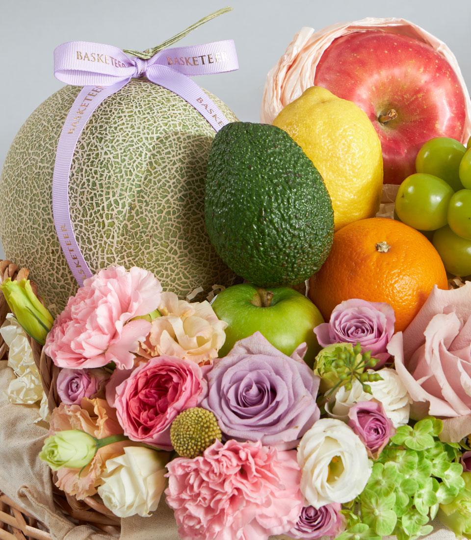 Pastel premium fruit and floral gift basket with fresh cantaloupe, apples, citrus, and pink roses for birthdays
