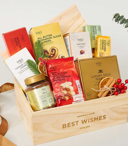 Wooden gift crate filled with premium M&S gourmet treats, coffee, and teabags, decorated with cinnamon and festive accents